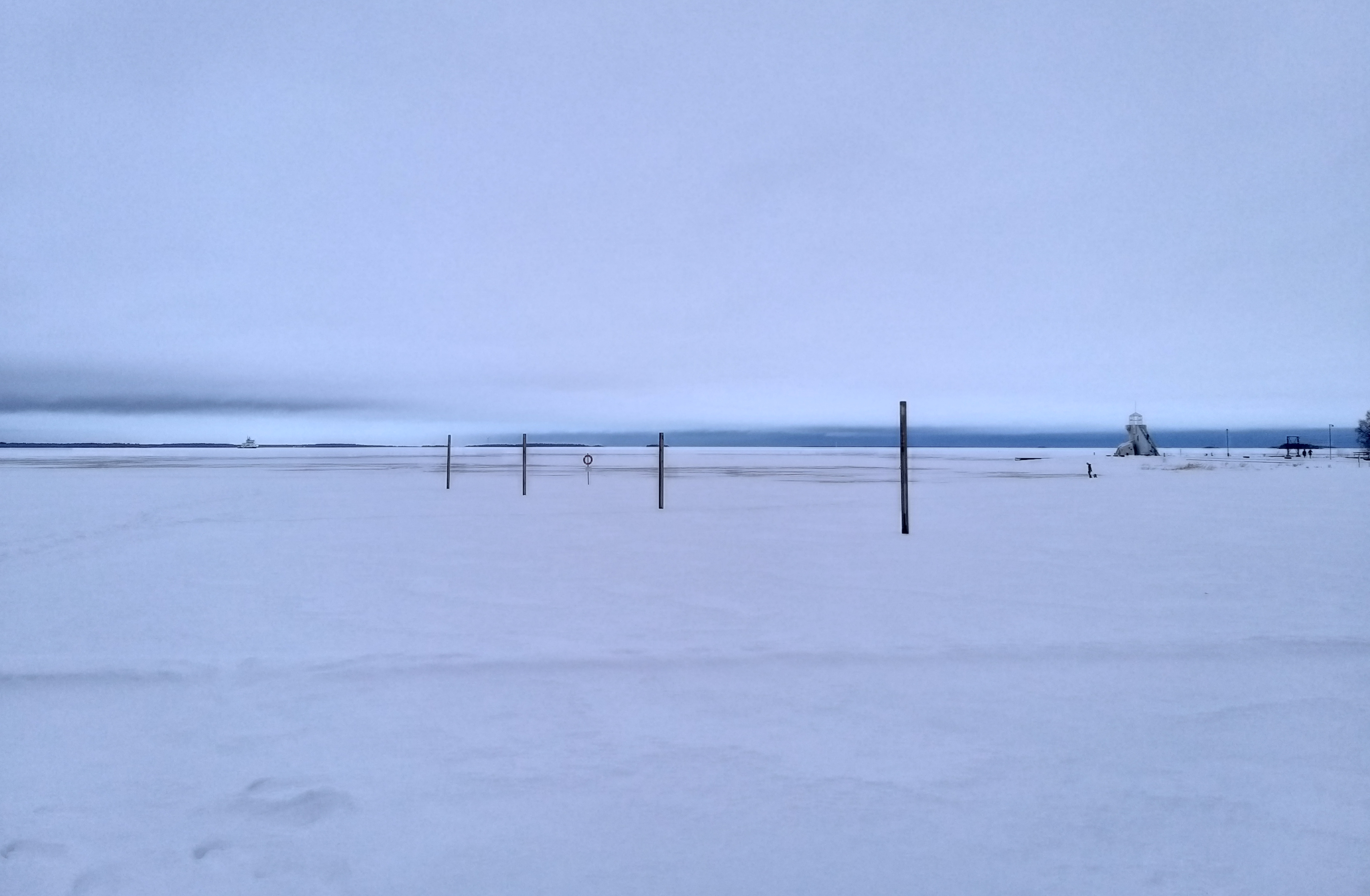 Nallikarin ranta talvella. Ulapalla laiva (jäänmurtaja?). Keskellä pystypaaluja, yhdessä pelastusrengas. Vasemmalla majakka ja muutamia ulkoilijoita.