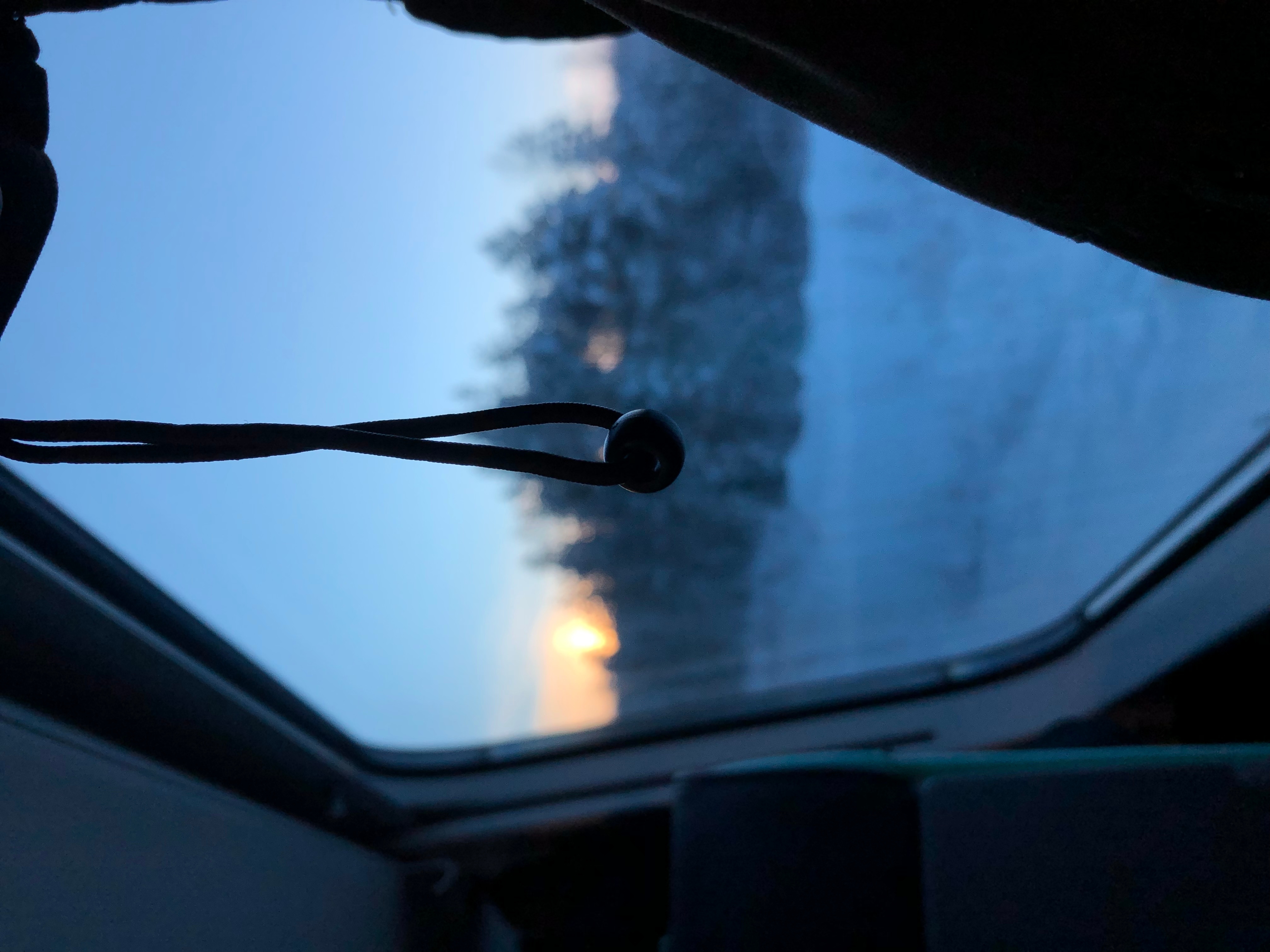 Narusilmukassa roikkuva muovihelmi. Taustalla (epäterävä) näkymä ulos junan ikkunasta: metsän reunaa ja horisontissa hieman punertava aurinko. Kuva on 90 astetta kallellaan, jonka takia kokonaisvaikutelma vaikuttaa hieman silmältä.