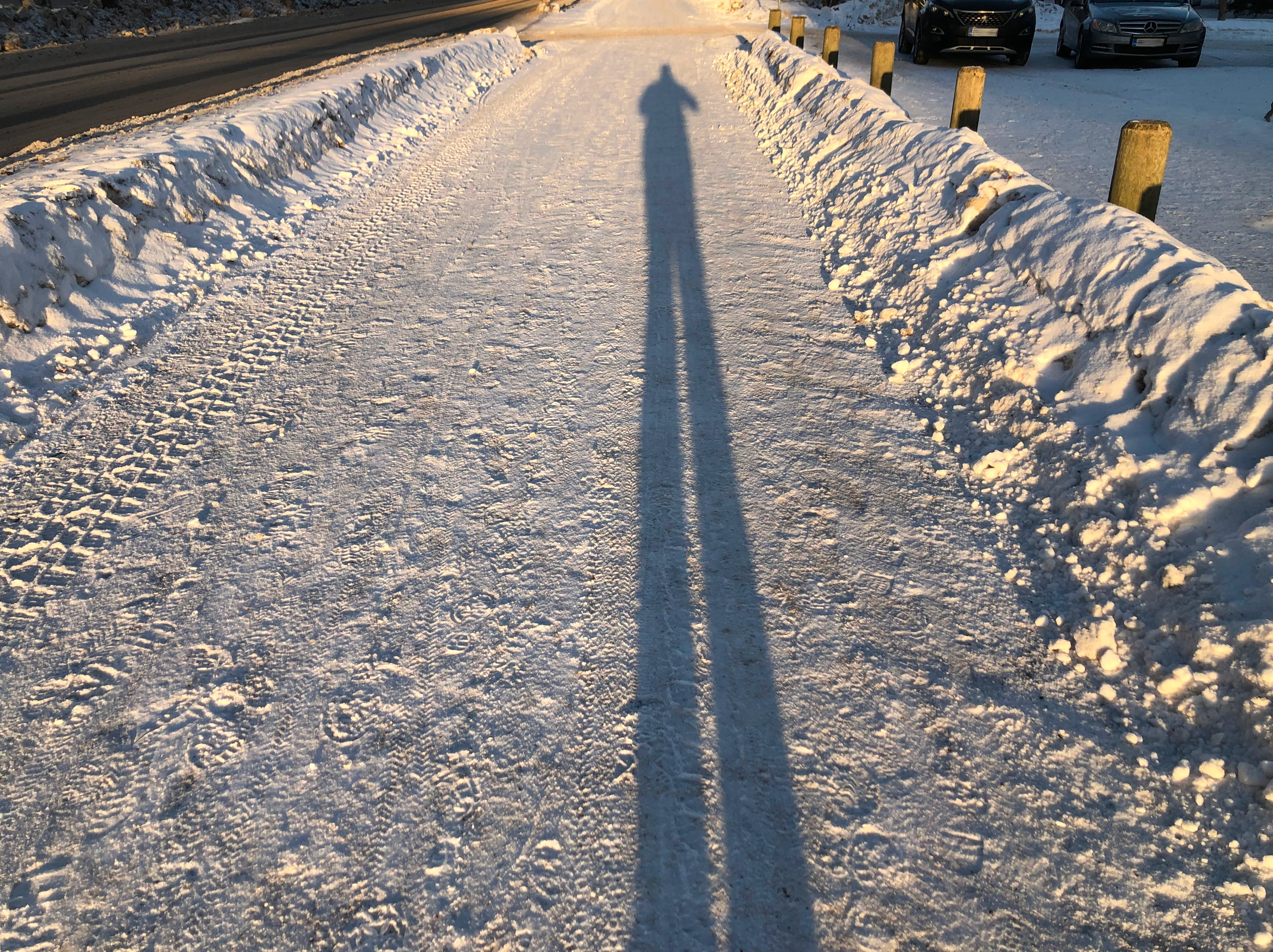 Kuvan ottajan piiitkäjalkainen varjo auratulla jalankulku- ja pyörätiellä.