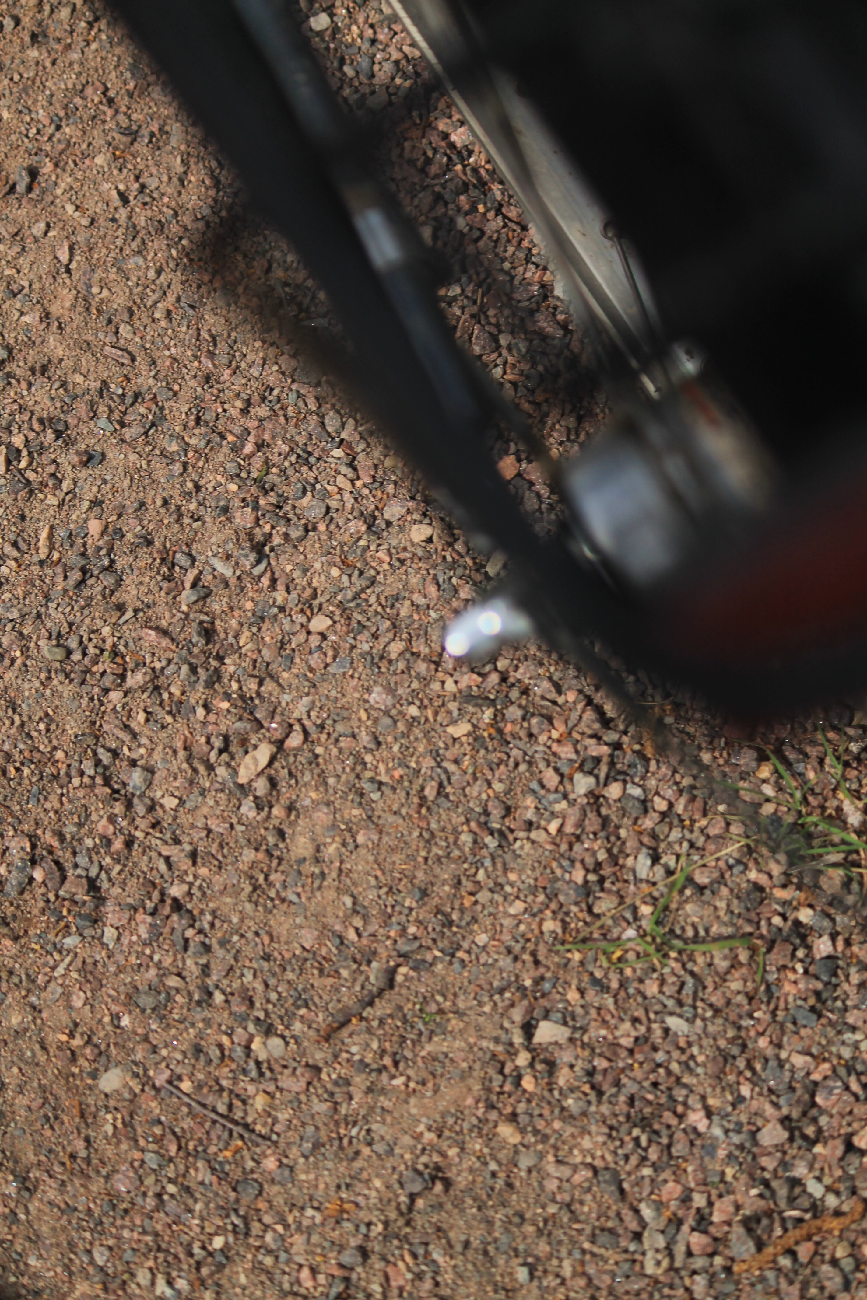 Näkymä polkupyörän takarenkaan yläpuolelta alas hiekkatielle. Shimanon Nexus 3-vaihdenapa epäterävänä oikealla.