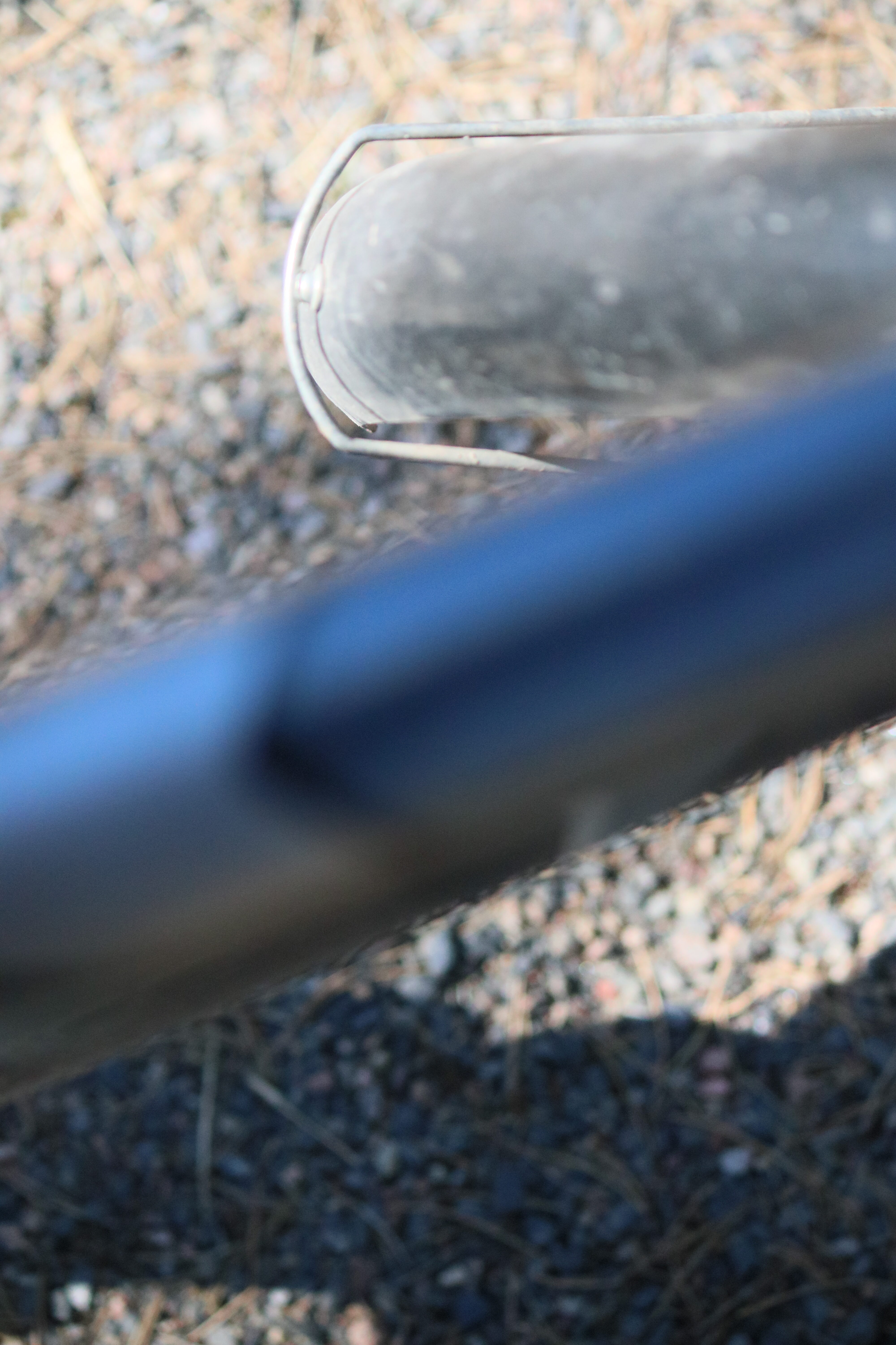 Polkupyörän runkoa ylhäältä päin: epäterävä pätkä siniharmaata vaakaputkea kulkee vasemmalta viistottain yläoikealle. Sen takana yläoikealla pätkä pölyn harmaannuttamaa, mustaa etulokasuojan takakaarta kiinnikerautoineen. Taustalla hiekkatien pohjaa, jota kuvan alaosassa peittää varjo.