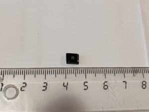 R-kirjainnäppäimen muotoinen ja näköinen, musta ja nelikulmainen muovinkappale viivottimen yläpuolella. Kappale on sivusuunnassa 6—7 mm pitkä, pystysuunnassa pari milliä lyhyempi.