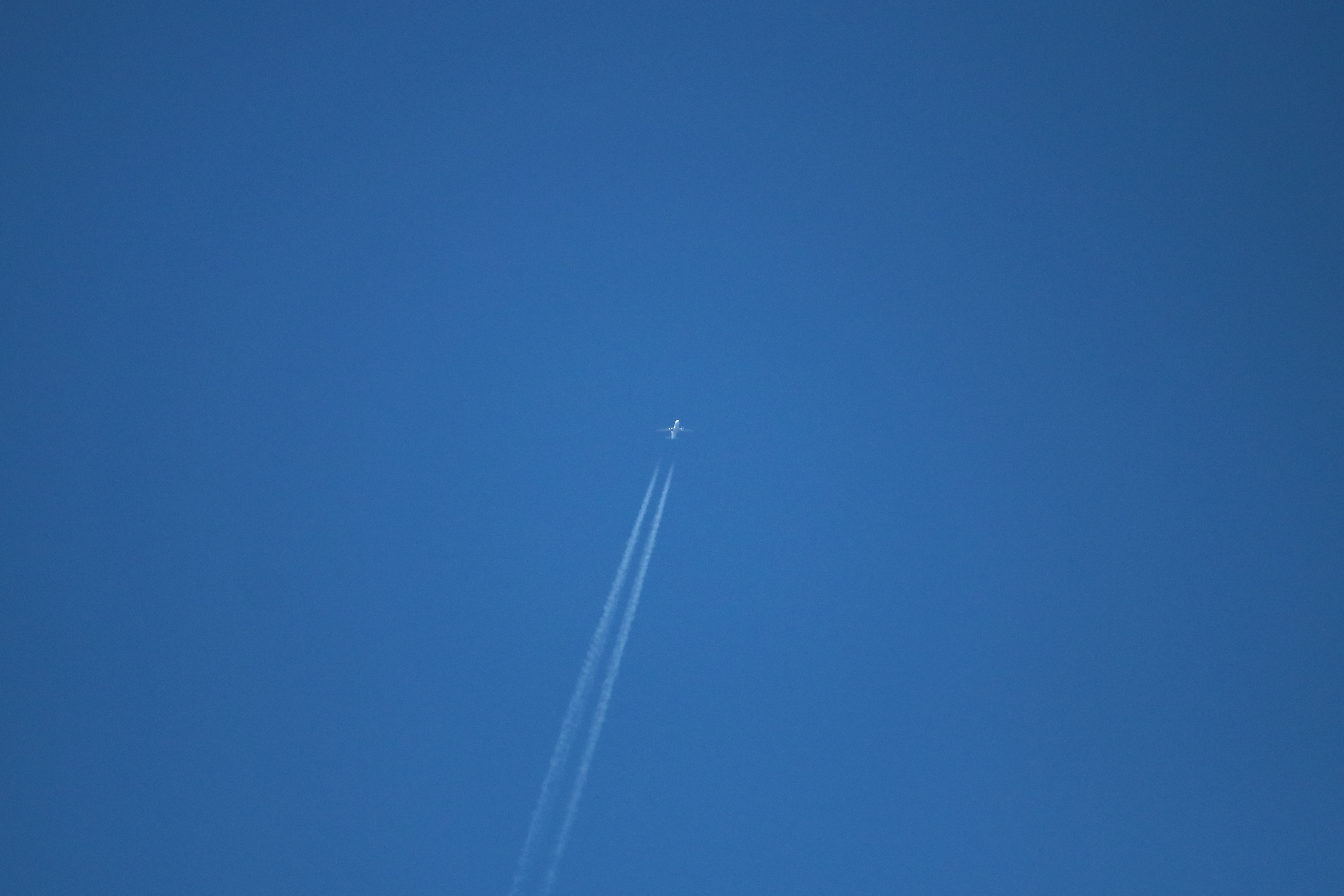 Suihkukone korkealla sinisellä taivaalla, perässään kaksi tiivistymisjuovaa.
